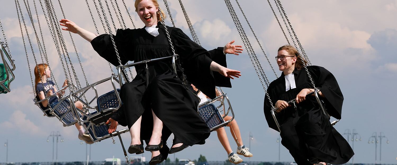 Drei Pfarrerinnen mit schwarzem Talar schweben auf einem Kettenkarussel in der Luft