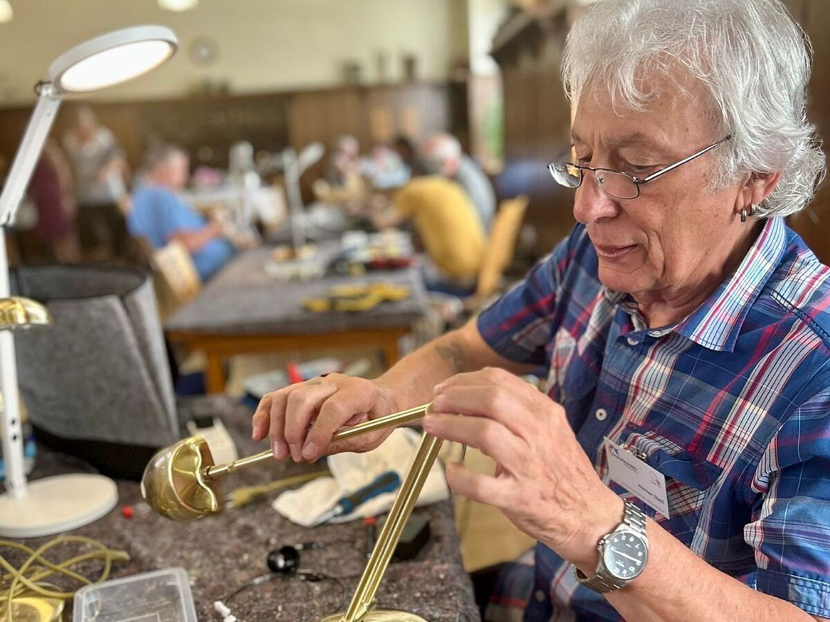 Ein Herr mit grauem Haar und Brille repariert eine goldene Messinglampe
